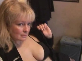 A mature woman with large breasts removes her clothes while wearing stockings and a mini skirt